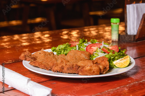 Fotografie, Obraz A plate of milanesa with salad on a wooden table.
