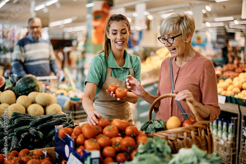 Print op canvas Happy sales clerk assists senior woman in buying vegetable at supermarket