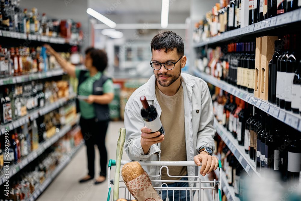 Young smiling man buying wine in supermarket.
