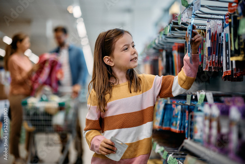 Tableau sur toile Smiling schoolgirl choosing products at school supplies section in supermarket