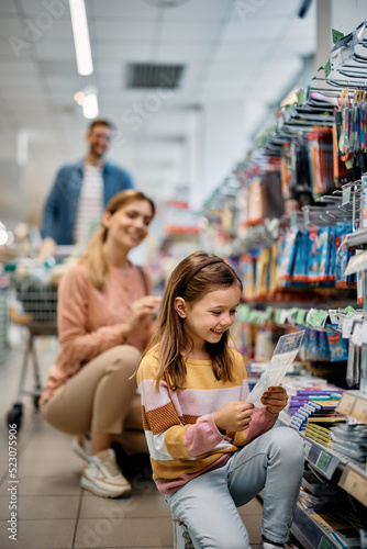 Fotografie Happy little girl shopping school supplies with her parents in store