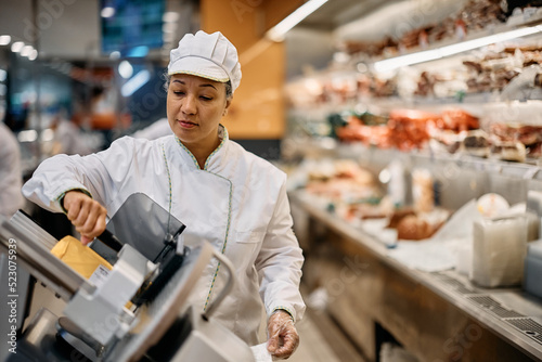 Supermarket worker using slicer at delicatessen section. photo