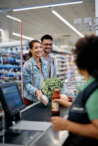 Young happy couple talks to cashier at supermarket checkout. photo