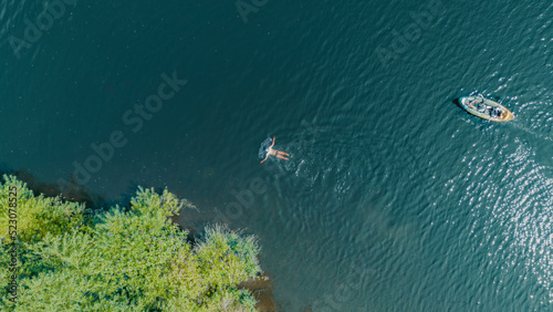 A man swimming and a couple paddling a kayak down a river with turquoise water. Aerial view from a drone.