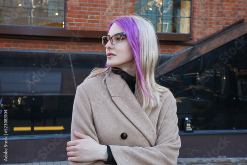 blonde with lilac strands of hair in a beige coat and glasses on the street