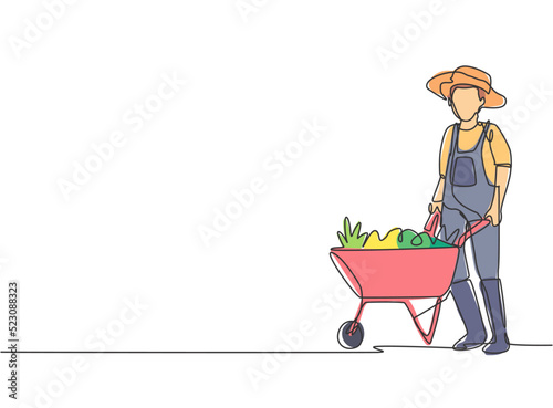 Single one line drawing of young male farmer standing beside the wheelbarrow trolley filled with fruits. Farming challenge minimalist concept. Continuous line draw design graphic vector illustration