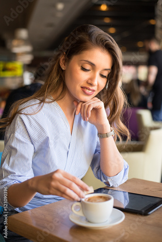 Young woman in cafe using tablet and drinking coffee