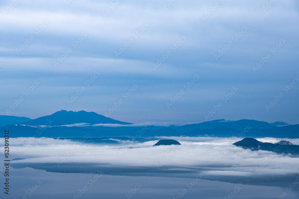 曇り空の下靄の流れる地上を見下ろす風景。日本の北海道の津別峠で。