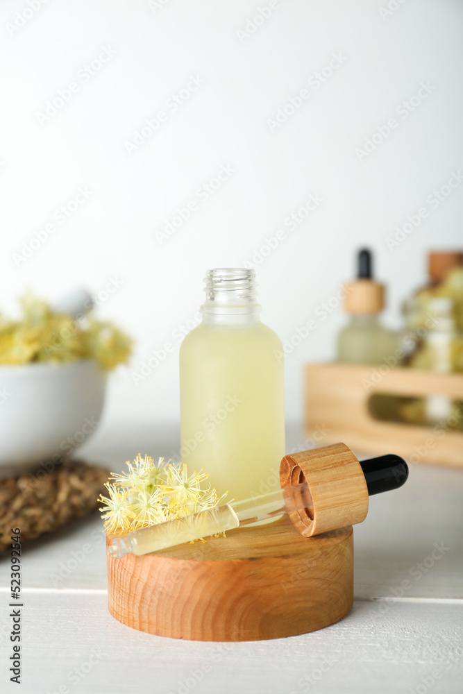 Bottle of essential oil and linden flowers on white wooden table Bottle of essential oil and linden flowers on white wooden table