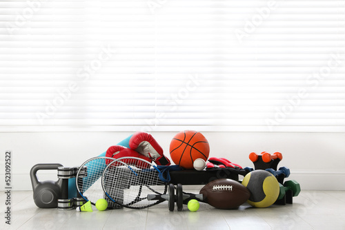 Set of different sports equipment on white floor indoors, space for text