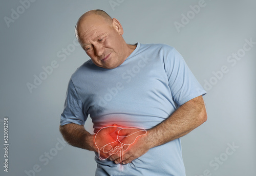 Mature man suffering from liver pain on light grey background photo