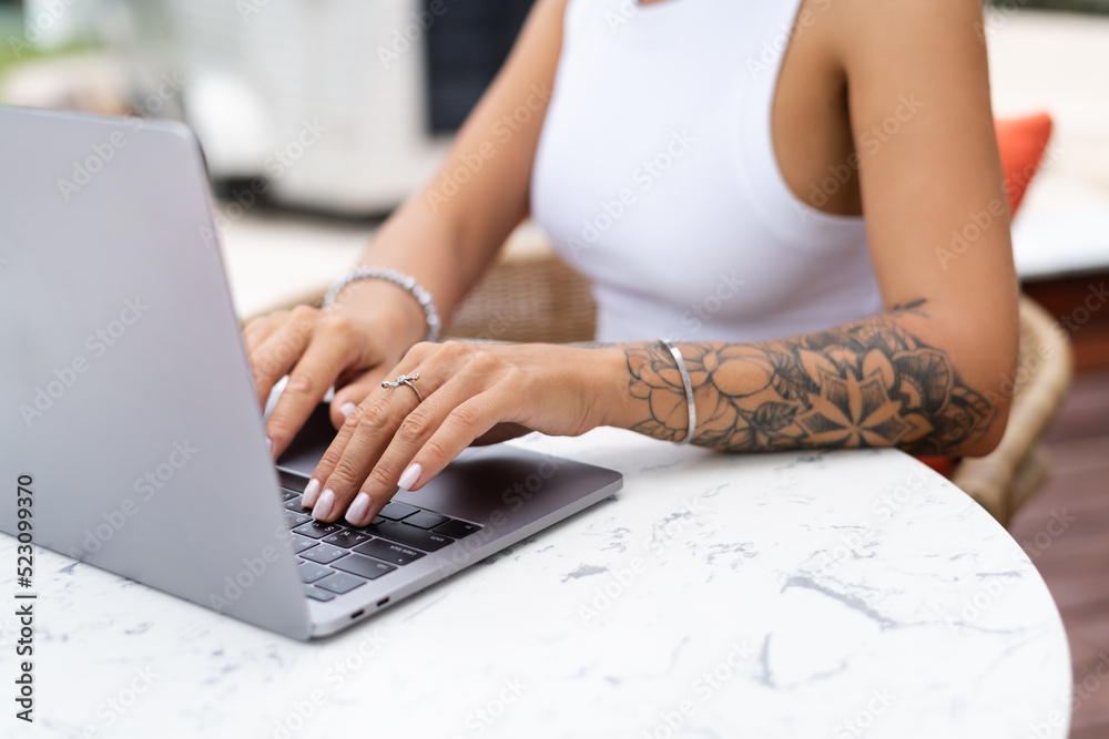 Fototapeta premium Beautiful young female hipster freelancer working with a laptop in a street cafe, writing an article, concentrated on work, close shot of hands