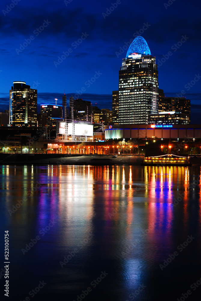 The lights of the Cincinnati skyline are reflected in the waters of the Ohio river while the city skyscraper buildings are illuminated against the night sky
