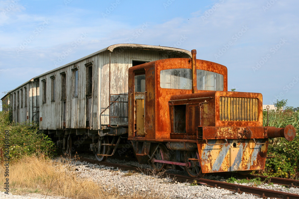 Vecchio treno arruginito  e abbandonato, su binario, composto da locomotore diesel e vecchi vagoni di legno.