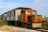 Vecchio treno arruginito  e abbandonato, su binario, composto da locomotore diesel e vecchi vagoni di legno.
