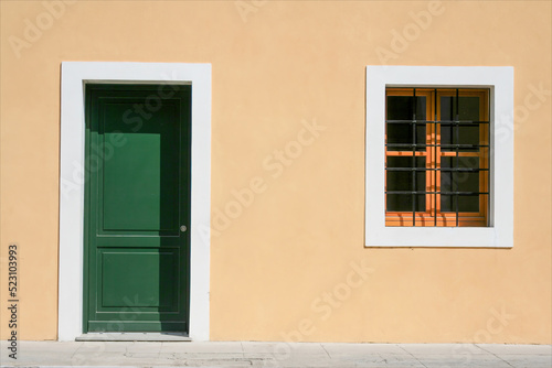 Facciata di edificio nuovo, casa  appena restaurata, composta da una finestra sbarrata e una porta verde con muro giallo. photo