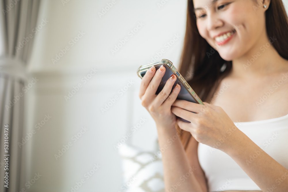 Happy and cheerful woman is using a phone sitting on a sofa.Asian young woman looking mobile phone celebrating with good news or discount voucher for shopping online at home. Happy and cheerful woman is using a phone sitting on a sofa.Asian young woman looking mobile phone celebrating with good news or discount voucher for shopping online at home.