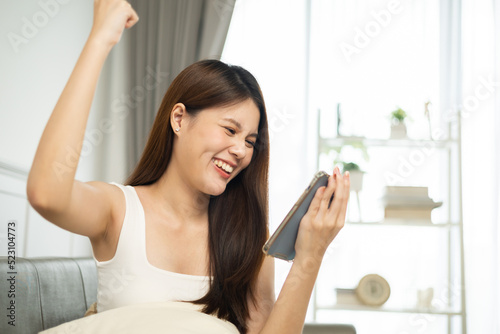 Happy and cheerful  asian woman looking on cellphone app read message feel excited.young woman looking mobile phone celebrating with good news or discount voucher for shopping online on sofa at home
