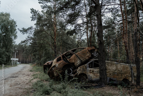 Burnt cars in the city of Irpin stand on the side of the road near a pine forest