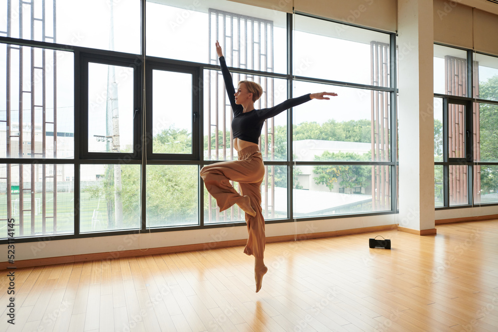 Talented young woman dancing to music in spacious studio