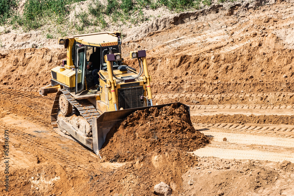 A powerful bulldozer in a sand pit is planning a site. Extraction of sand in an open pit. natural building materials. A powerful bulldozer in a sand pit is planning a site. Extraction of sand in an open pit. natural building materials.