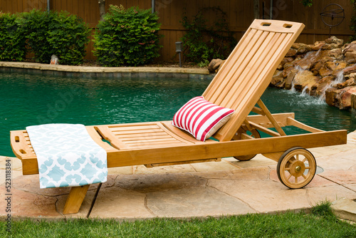 Wood chase lounge chair on a pool deck with swimming pool in the background.