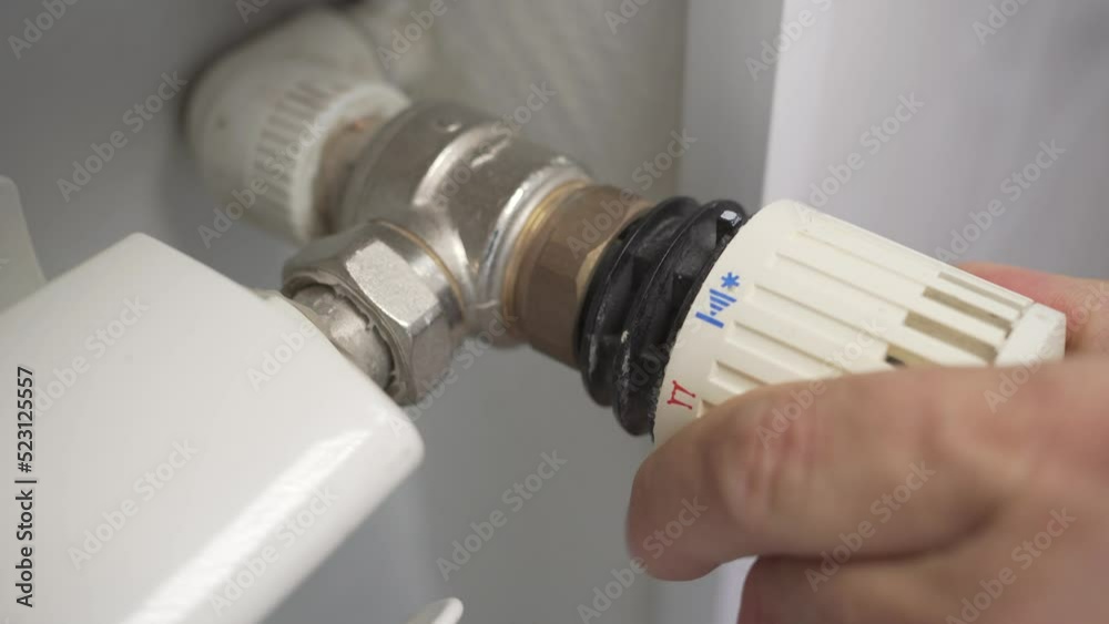 Man adjusts the temperature of the battery. Thermostat for fixing and limiting the temperature setting in heating radiators. Man adjusts the temperature of the battery. Thermostat for fixing and limiting the temperature setting in heating radiators.
