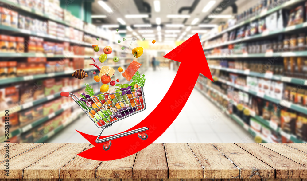 Fototapeta premium Food cost rising concept. Shopping cart full of groceries and red arrow pointing up