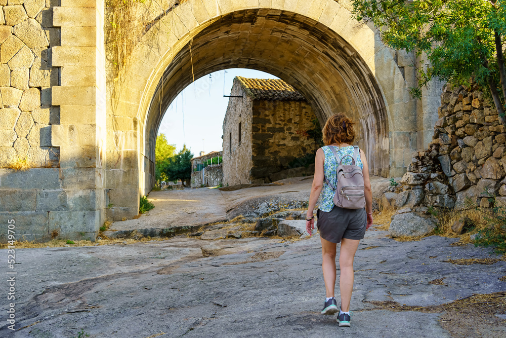 Tourist woman crossing an old stone bridge at the entrance of a village in Castile, Puente Congosto.