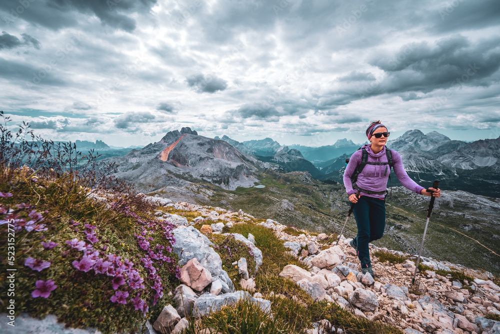 Young woman is hiking on beautiful trail with flowers from Baires Lake to Seekofel in the Dolomite mountains in the morning. Seekofel, Dolomites, South Tirol, Italy, Europe.