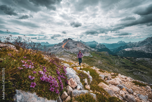 Young woman is hiking on beautiful trail with flowers from Baires Lake to Seekofel in the Dolomite mountains in the morning. Seekofel, Dolomites, South Tirol, Italy, Europe. photo