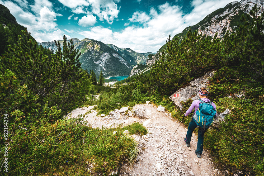 Young woman is hiking on beautiful trail Seekofel to Baires Lake in the Dolomite mountains in the afternoon. Braies Lake (Pragser Wildsee, Lago di Braies), Dolomites, South Tirol, Italy, Europe.
