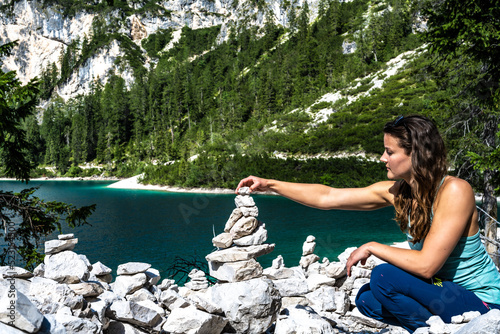 Young woman builds stone man with Baires Lake in the background.. Braies Lake (Pragser Wildsee, Lago di Braies), Dolomites, South Tirol, Italy, Europe. photo