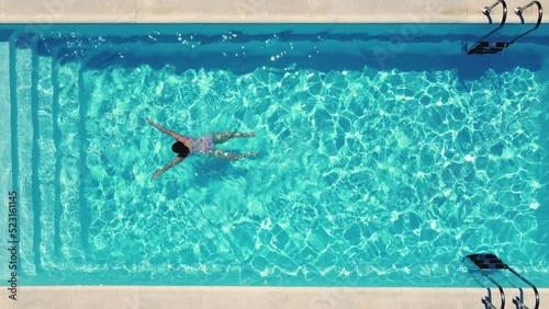 Top view of a young caucasian woman, swimming relaxed in a crystal clear pool. Concept holidays, travel, summer, 4k resolution.
