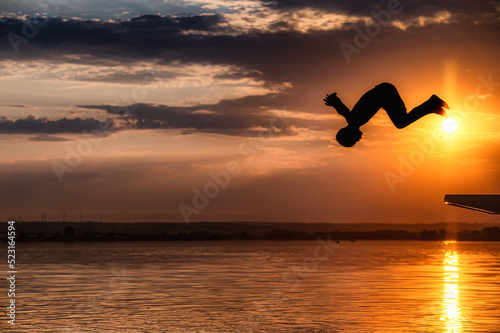 Junge springt kopfüber in einen See während im Hintergrund die Sonner untergeht