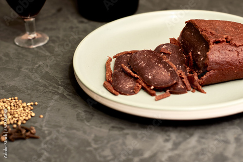 sliced basturma on a plate next to a bottle of wine and a glass