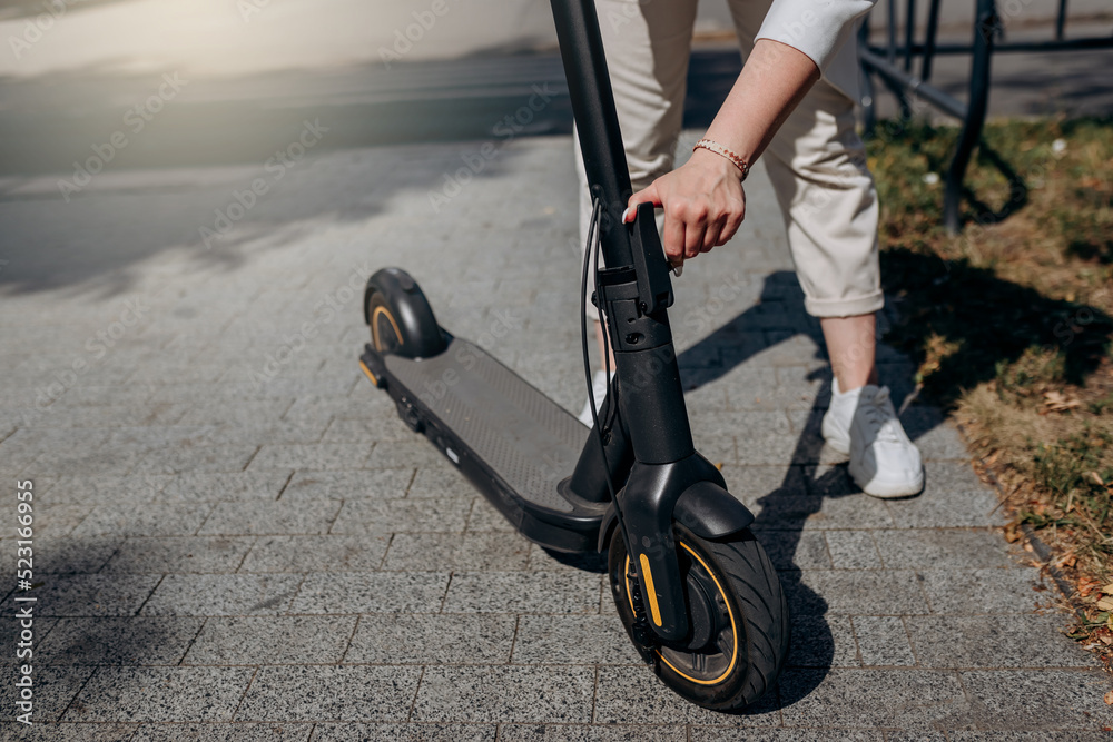 Obraz premium Close up of woman in white suit folding her electro scooter after ride while standing in city parkland