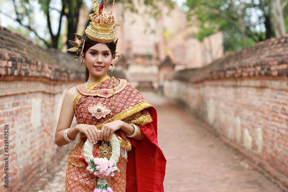 Young fashion and beautiful asian woman wearing Thai red traditional costume holding jasmine flower garland with happy and peace standing outdoor in ancient temple Ayutthaya, Thailand. Travel concept