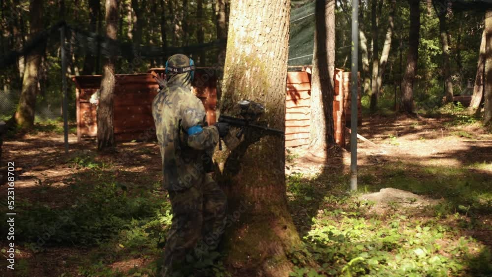 A young man is playing paintball with his friends, wearing camouflage and a protective mask, taking part in leisure activities. A young man is playing paintball with his friends, wearing camouflage and a protective mask, taking part in leisure activities.