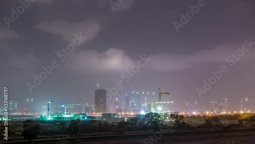 Skyline of construction cranes tower with skyscrapers on background in the Middle East day to night transition timelapse, Dubai. Evening mist. Cloudy sky photo