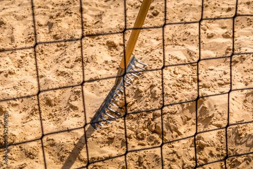 ein Netz vor dem Volleyball Platz verdeckt den Rechen der auf dem gelben Sand steht