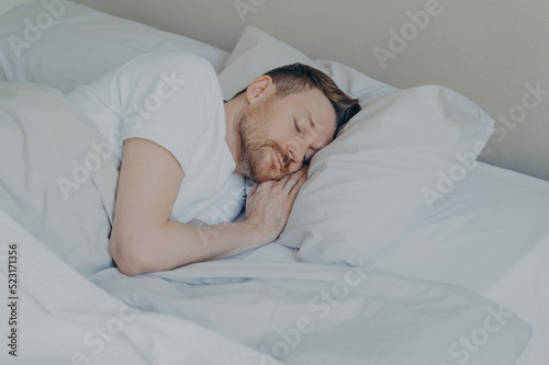 Handsome young man comfortably sleeping in bed at home