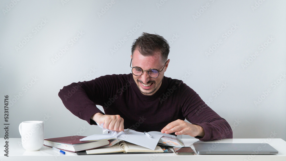 Angry man working in office tears out a piece of paper from a notebook - wrong entries Angry man working in office tears out a piece of paper from a notebook - wrong entries