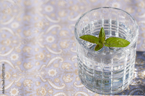 sprudelndes Wasser in einem durchsichtigen Glas mit einem Minzblatt auf einer gemusterten Tischdecke 