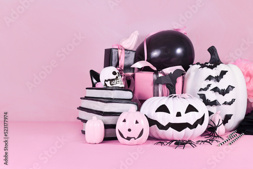 Pink Halloween decor with black and white pumpkins, spell books and spiders with copy space