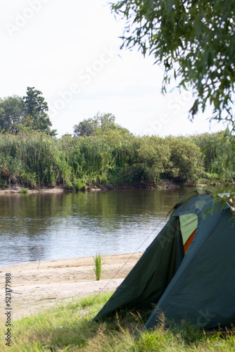 Tent camp on the river bank. A fragment of the tent is visible. Medium plan.