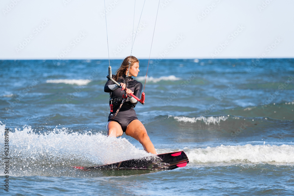 Kite surfing girl in swimsuit with kite in the sky rides the waves with splashing water. Water sports, sporty woman, action concept and hard sport