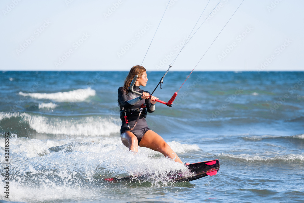 Kite surfing girl in swimsuit with kite in the sky rides the waves with