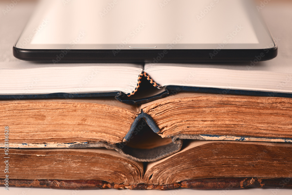 Open pages of old shabby brown and new books, digital tablet. Concept of choice between new technologies and old books. Analog vs digital. Closeup.