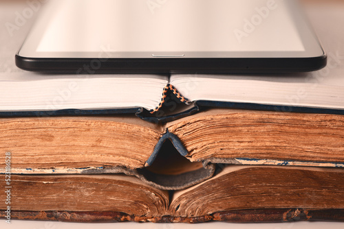 Open pages of old shabby brown and new books, digital tablet. Concept of choice between new technologies and old books. Analog vs digital. Closeup.